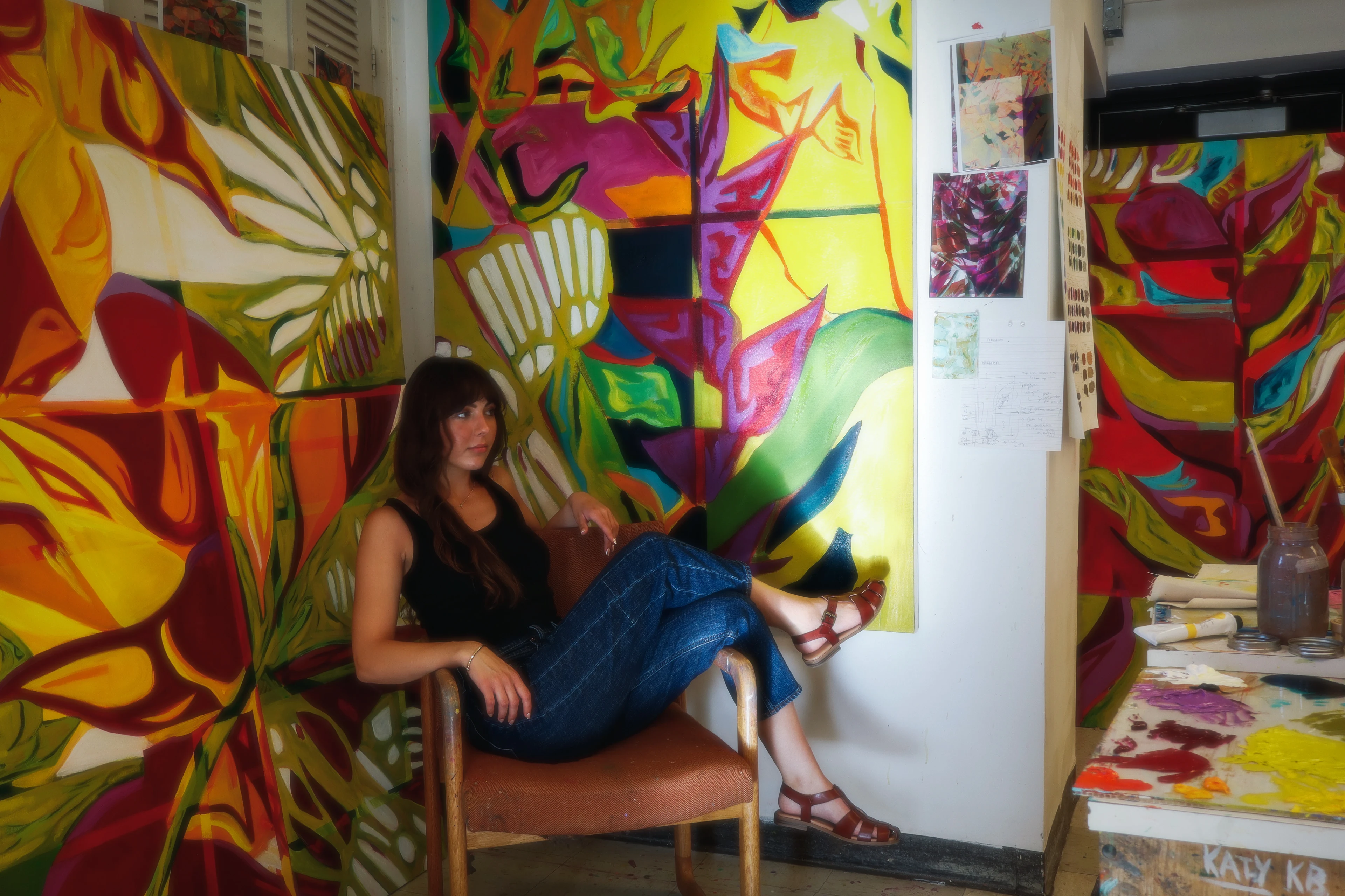 Mia Baker lounging in her studio, surrounded by large-scale Terrarium oil paintings.